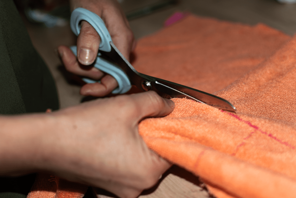 decoupe-tissu Une main et une paire de ciseaux découpant un tissu feutré orange.